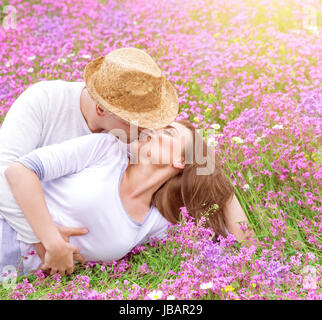 Romantische Küsse im Freien, attraktiven Mann küssen seine schöne junge Frau liegend auf rosa Blumen Wiese, Frühling Zeit Konzept Stockfoto