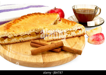 Apfelkuchen mit Zimt klebt auf einem runden Holzbrett, einen ganzen Apfel, Serviette, Tee in die braune Tasse mit zwei Stück Zucker, zwei Scheiben Apfel isoliert auf weißem Hintergrund Stockfoto