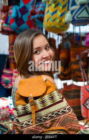 Schöne Frau tragen Backpacke, ein Anden traditionelle Kleidung Textil Garn und Gewebe von Hand im Hintergrund Wolle, bunte Stoffe. Stockfoto