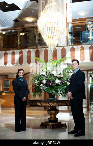 Elegant gekleidet Front-Office Manager posiert unter einem Chandler mit Blumenvase als Herzstück Stockfoto