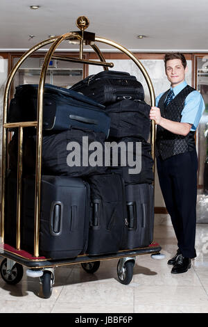 Gut aussehend männlichen Concierge posiert mit einem Haufen von Taschen im Gepäckwagen Stockfoto