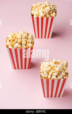 Popcorn in roten und weißen Karton auf rosa Hintergrund. Stockfoto