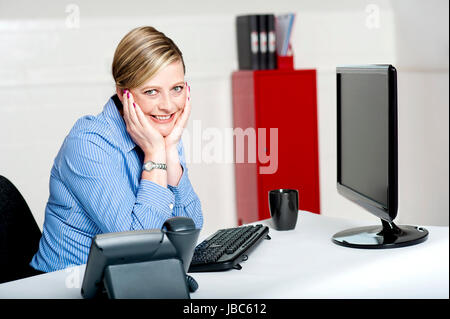 Charmante corporate Lady posiert im Amt. Mit den Händen auf ihre Wange sitzen Stockfoto