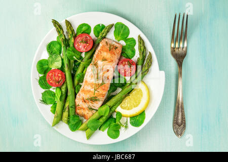 Eine obenliegende Foto einer Platte gegrillter Lachs mit grünem Spargel, Kirschtomaten, Feldsalat und einer Scheibe Zitrone, eine gesunde Ernährung-Schale mit einer pla Stockfoto