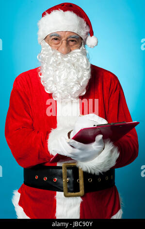 Vater Nicholas Vorbereitung eine Liste der Geschenkempfänger in Zwischenablage. Isoliert auf blau. Stockfoto