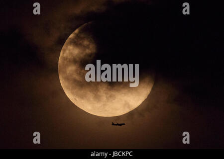 Ein Flugzeug fliegt Vergangenheit der Erdbeere Mond über Tokyo City am 10. Juni 2017, Japan aufgeht. Es ist ein astronomisches Phänomen, das in dieser Zeit des Jahres, tritt auf, wenn der Mond am nächsten an den Horizont und leuchtet in einem rötlichen Ton. Erdbeere Mond ist benannt nach der Erdbeeren pflücken-Saison im Juni beginnt. Bildnachweis: Rodrigo Reyes Marin/AFLO/Alamy Live-Nachrichten Stockfoto