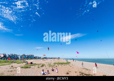 Menschen auf stoney Strand in Walmer, Deal, in Kent, England sitzen während Drachen fliegen. Verschiedene Drachen fliegen im blauen Himmel. Stockfoto