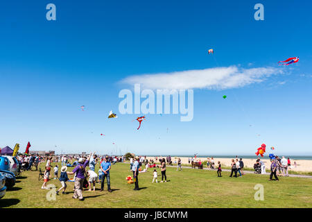 Menschen versammelt, auf Gras von Strand in Walmer in Kent, England, als Teil eines Drachen fliegen. Blauer Himmel mit verschiedenen Drachen fliegen. Stockfoto