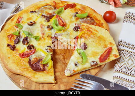 Hausgemachte Pizza mit geräucherter Wurst, Oliven, Tomates, Käse und Basilikum auf Olivenöl Holz Schneidebrett. Stockfoto