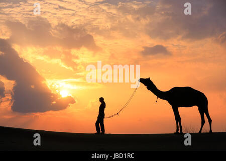 Silhouette Person mit einem Kamel bei Sonnenuntergang, Thar-Wüste in der Nähe von Jaisalmer, Rajasthan, Indien Stockfoto