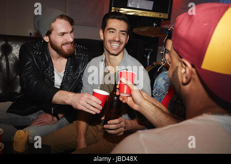 Gruppe von lächelnden jungen Menschen Anhebung Biergläser hanging out auf Party und Spaß haben Stockfoto