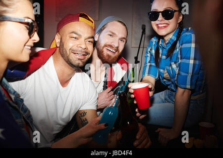 Gruppe von lächelnden jungen Party-People, Männer und Frauen, Bier trinken und Erhöhung der Brille hängen in Nachtclub Stockfoto