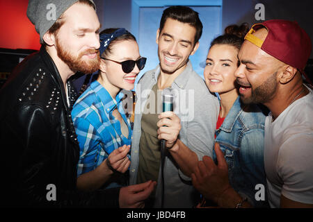 Gruppe des Lächelns Partypeople, Männer und Frauen, stehen auf der Bühne singen zu Mikrofon bei Nacht Club party Stockfoto