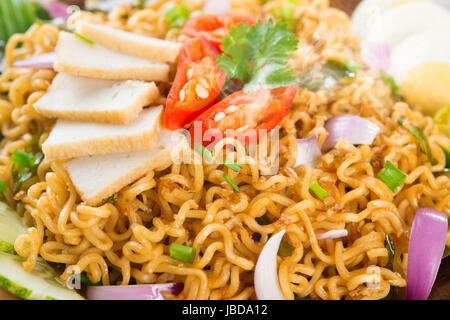 Nahaufnahme von trockenen Instantnudeln, malaysischen Stil Maggi Goreng Mamak oder würzige trockene Curry-instant-Nudeln. Asiatische Küche, Esstisch aus Holz Einstellung servierfertig. Frisch heiß mit gedünstetem Rauch. Stockfoto