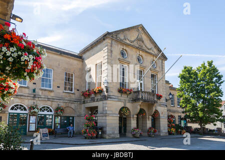 Das Rathaus in Brunnen auf dem gepflasterten Marktplatz steht und fällt im reizvoll Blumenschmuck im Sommer, Somerset, England, UK Stockfoto