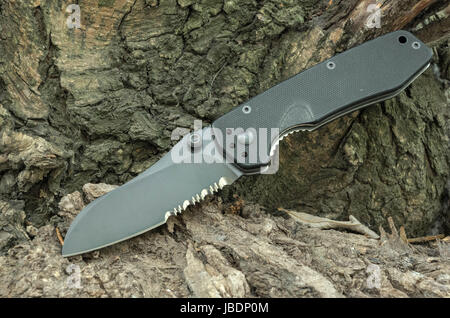 Schwarze Messer auf einer Baumrinde. Taschenmesser. Tourist-Messer. Stockfoto