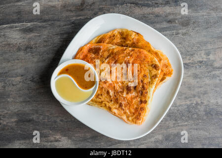 Indische Roti Prata mit Kondensmilch und Curry-Sauce, Nahaufnahme von rustikalen indischen Roti gebratenen Pfannkuchen Stockfoto