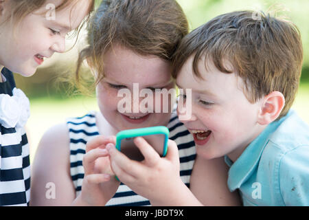 Glücklich lachende Kinder spielen mit Smartphone außen Stockfoto