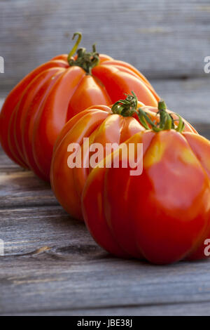 Drei große Fleischtomaten hintereinander frisch vom Wochenmarkt auf einem alten Holztisch Stockfoto