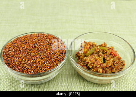 Ungekochte rote Quinoa Samen in eine Runde klaren Glasschale neben eine schmackhafte und gesunde Vorspeise Schale gekochte Quinoa mit Jalapeno Scheiben Tomaten und Parmesan-Käse auf einem grünen Tischset gemischt. Stockfoto