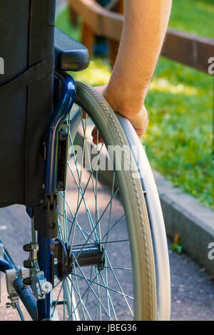 Hand des jungen Mannes auf dem Rad des Rollstuhls im Stadtpark Stockfoto