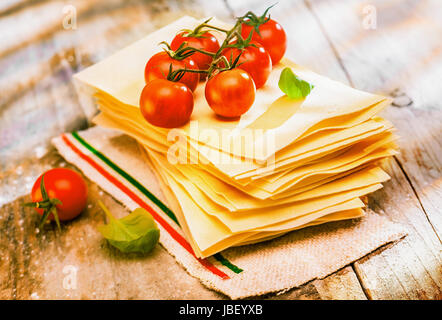 Italienische Lasagne mit frischen Reife rote Cherry-Tomaten und Basilikum auf Blättern von Trockenteigwaren stehen bereit auf einen alten rustikalen Holz Küchentisch vorbereiten Stockfoto