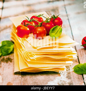 Getrocknete ungekochte Teigwaren Lasagneblätter mit frischen Zutaten wie Cherry-Tomaten und Basilikum-Blätter, hautnah alte Holzbretter Stockfoto