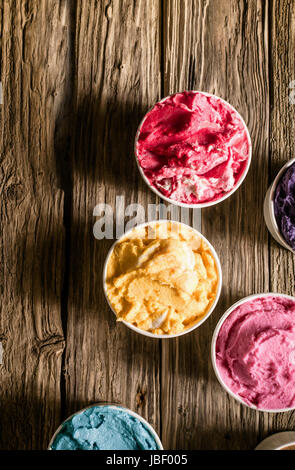 Auswahl an leckeren cremigen Eis von verschiedenen Geschmacksrichtungen und Farben in den einzelnen Wannen auf einem alten Holztisch mit Exemplar, Draufsicht serviert Stockfoto