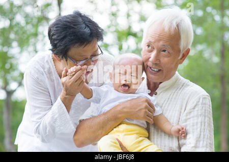Asiatische schreiendes Baby getröstet von Großeltern im Garten Stockfoto
