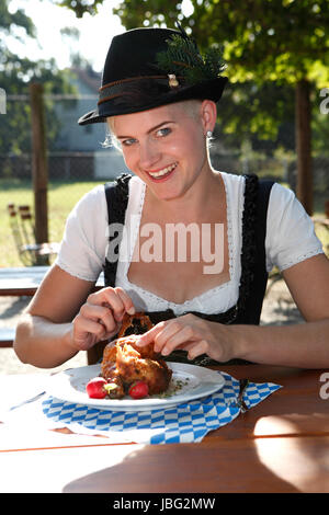 Blonde Mädchen isst halbe Hähnchen in einem traditionellen bayerischen Biergarten Stockfoto