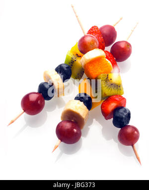 Vibrant fresh fruit kebabs for a healthy snack with assorted grapes, strawberries, blueberries, banana, kiwifruit and orange on wooden skewers on white Stockfoto