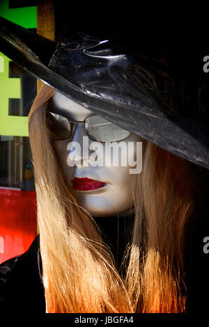 Eine Schaufensterpuppe mit Silber lackiert Gesicht und roten Lippenstift mit einem Hexen Hut und langen roten Perücke mit Sonnenbrille draußen ernst. Stockfoto