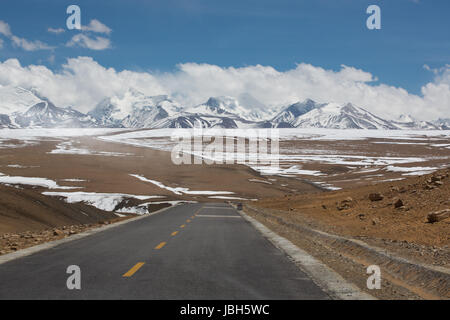 Gerade Straße mit einer gelben gepunkteten Linie in der Mitte mit tibetischen Landschaft der Berge im Hintergrund. Der Weg scheint zu gehen in Richtung der schneebedeckten Berggipfel in der Cloud. Stockfoto