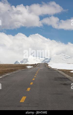 Gerade Straße mit einer gelben gepunkteten Linie in der Mitte mit tibetischen Landschaft der Berge im Hintergrund. Der Weg scheint zu gehen in Richtung der schneebedeckten Berggipfel in der Cloud. Stockfoto