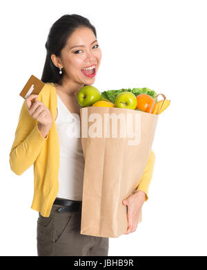 Glückliche junge Pan asiatische Frau mit Papier Einkaufstasche voller Lebensmittel und Kreditkarte isoliert auf weißem Hintergrund. Stockfoto