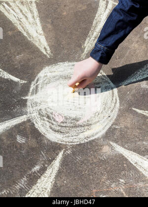 Mädchen Zeichnung eine Sonne mit farbiger Kreide auf Asphalt auf Straße Stockfoto