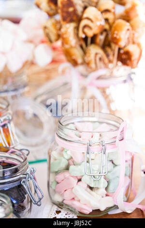 Nahaufnahme von Pastell farbigen Marshmallows in Glas mit Zierband mit kleinen Snack Size Zimtschnecken auf Stöcken in einem Glas im Hintergrund Stockfoto