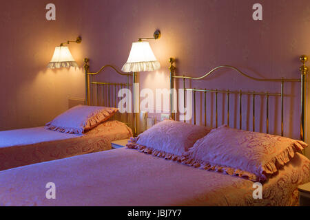 Trendiges Hotel in Rosa mit zwei Betten, im Lichte der Nachttischlampen und kaltes Licht aus dem Fenster. Stockfoto