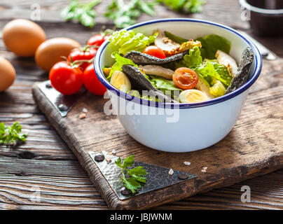 Schöne Cäsarsalat mit schwarzen Croutons auf einem Holzbrett. Stockfoto