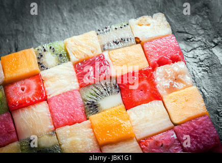 Gewürfelter Südfrüchte, angeordnet in einem dekorativen bunten Quadrat mit einer Nahaufnahme zeigt die Textur und Muster der Wassermelone, Kiwi, Ananas, Erdbeere und Melone auf einen Schiefer Zähler Stockfoto