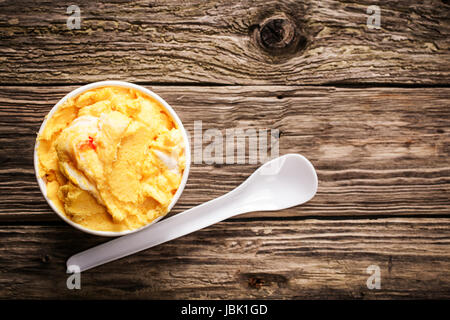 Take-away Wanne lecker erfrischend spritzige Zitrusfrüchte Eis oder Sorbet serviert mit einem Einweg-Plastik Löffel auf einem alten verwitterten strukturierte Holztisch mit Knoten und Exemplar, Draufsicht Stockfoto