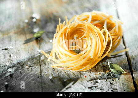 Getrocknete italienische Linguine oder Tagliatelle Nudeln in Spulen liegen auf einem rustikalen Grunge grau Holz Hintergrund mit Exemplar Stockfoto