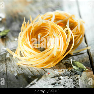 Ungekocht Spulen des italienischen Nudeln oder Tagliatelle Teigwaren aus getrockneten Hartweizen Weizenteig auf einem Grunge Holztisch, quadratischen Format Stockfoto