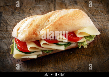 Köstliche Scheiben Gouda Käse mit Tomaten, Salat und Gurke auf einem knusprigen goldenen Baguette für gesunde vegetarische Küche Stockfoto