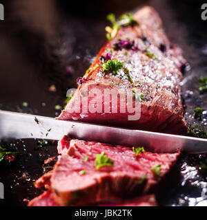 Schnitzen eine Portion leckere seltene Braten Rinderfilet Filet gewürzt mit frischen Kräutern mit einem großen Stahl Tranchiermesser Stockfoto