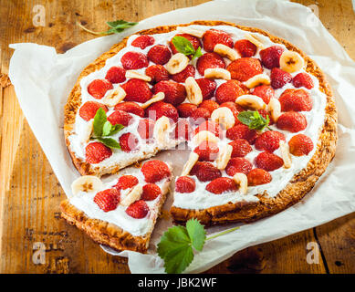 Frisch gebackene Erdbeeren und Bananen-Flan mit einer goldenen Kruste und Topping von frischen Beeren, Bananen und Sahne garniert mit Pfefferminze auf ein Quadrat aus weißem Papier, hoher Winkel anzeigen Stockfoto