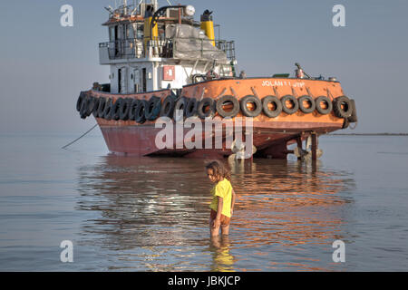 Bandar Abbas, Hormozgan, Iran - 16. April 2017: ein kleines iranische Mädchen in ein gelbes T-shirt, etwa sieben Jahre alt, Spaziergänge am Wasser in flachen Gewässern Stockfoto