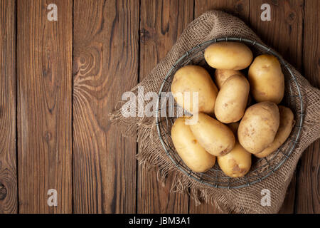 Frische Kartoffeln im Korb auf alten hölzernen Hintergrund. Ansicht von oben Stockfoto