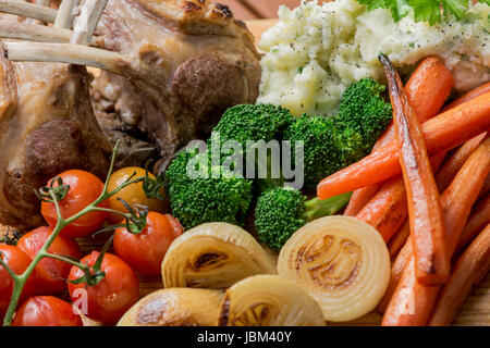 Gebratenes Lammkarree mit gebratenem Gemüse, Zwiebeln, Karotten, Tomaten, Brokkoli und Kartoffelpüree Stockfoto