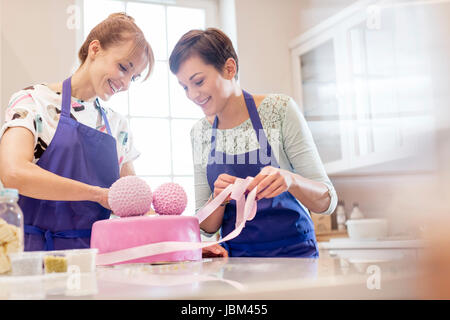 Weibliche Caterer Veredelung rosa Hochzeitstorte in Küche Stockfoto